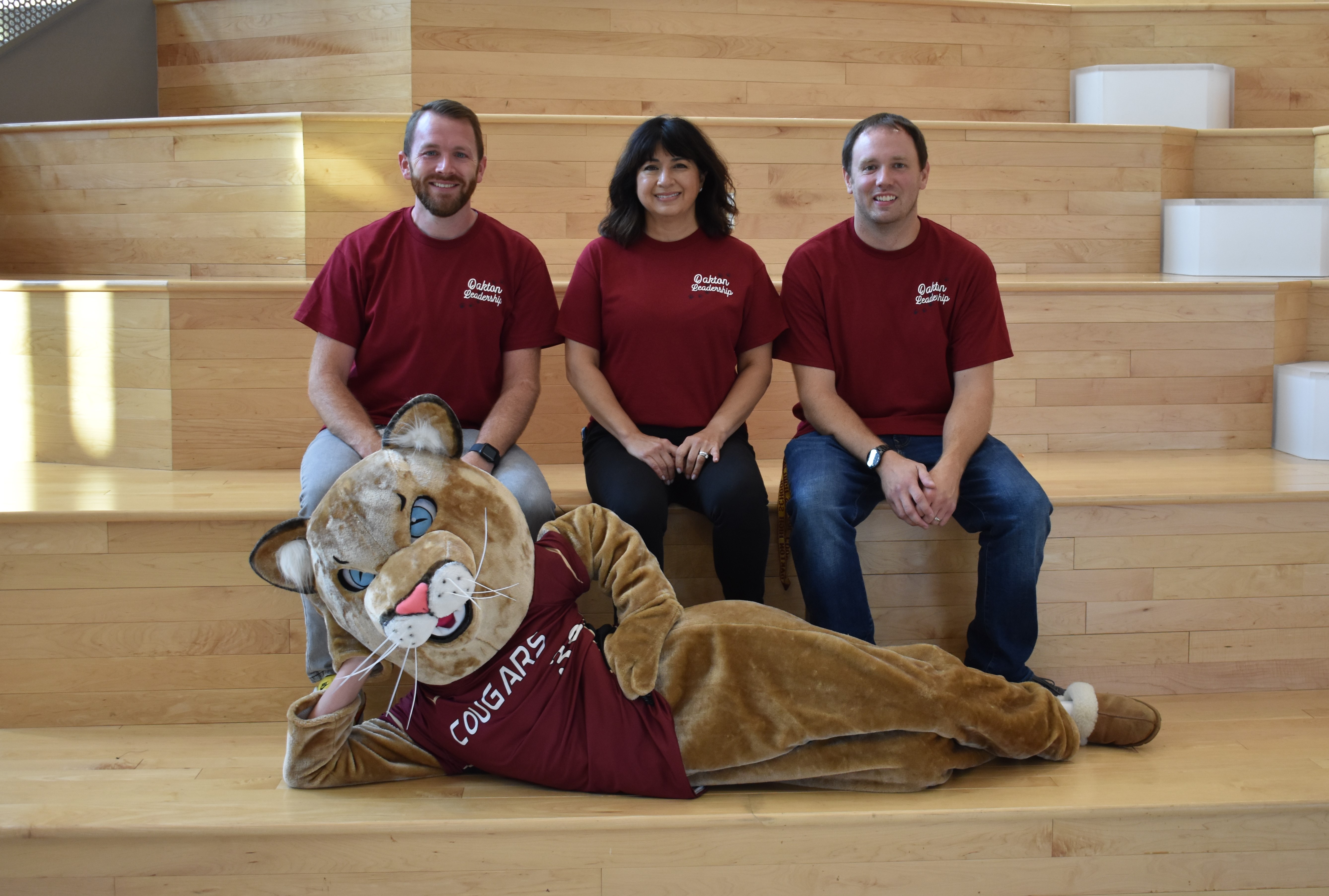 image of Mr. Farrell, Ms. weber, and Mr. McCulla on stairs with the Oakton Cougar mascot lying on the stairs in front of them